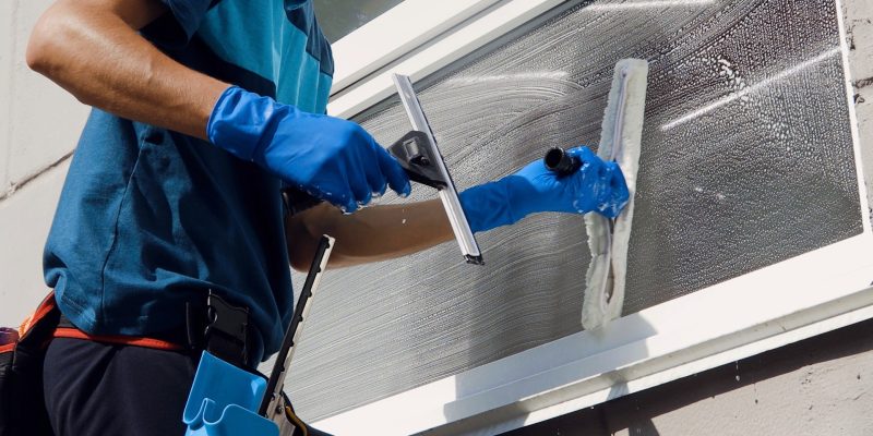 Reinigungsfachmann mit Reinigungsausrüstung säubert Fenster.