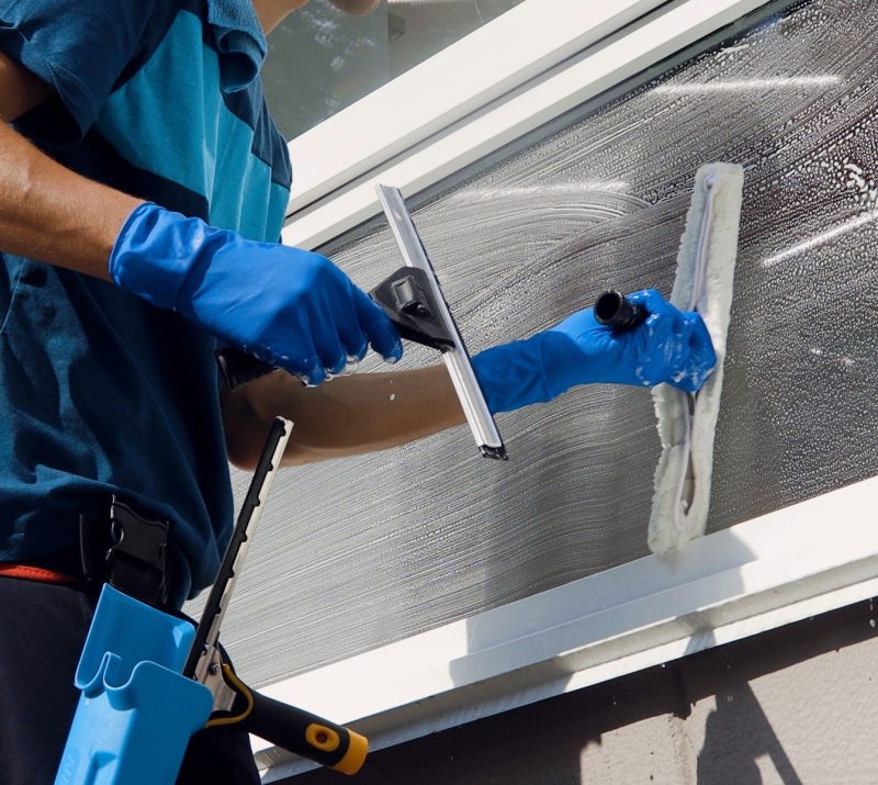 Reinigungsfachmann mit Reinigungsausrüstung säubert Fenster.