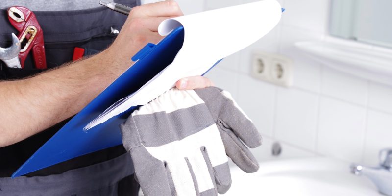 Hausmeister steht in Badezimmer mit einem Klemmbrett und dokumentiert